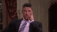 a man in a suit and tie is sitting in a chair with his hand on his face .