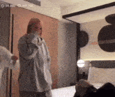 a woman is standing in front of a bed in a hotel room laughing .