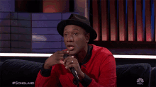 a man sitting on a couch holding a microphone with the nbc logo on the bottom