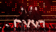 a group of women are sitting on a stage in front of a red background