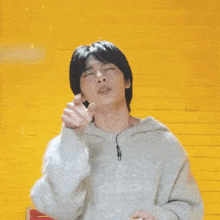 a young man with his eyes closed is wearing a gray sweater and a ring on his finger