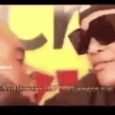 a man wearing sunglasses is talking to another man in front of a yellow and red star .