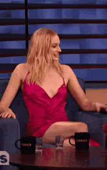 a woman in a pink dress sits at a table with two conan coffee mugs