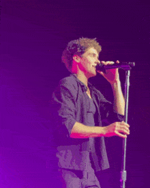 a man singing into a microphone with a purple background