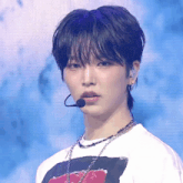 a young man wearing a white shirt and a microphone looks at the camera
