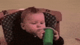 a baby in a high chair is drinking from a green cup .