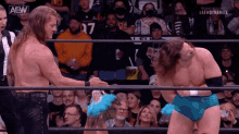 two wrestlers are shaking hands in front of a crowd while standing in a ring .