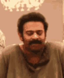 a man with a mustache and beard is standing in front of a chandelier .