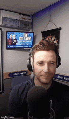a man wearing headphones stands in front of a microphone in front of a screen that says " the big show "