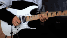 a man is playing a white electric guitar with a black and white sweater on