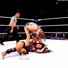two women are wrestling in a ring with a referee in the background .