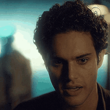 a close up of a man 's face with curly hair looking at the camera in a dark room .