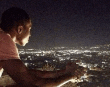 a man in a pink shirt looks out over a city at night