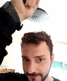 a man with a beard holds up a shower head