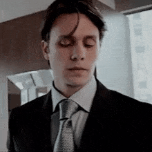 a man in a suit and tie is standing in front of a window with his eyes closed .