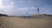 a blue rocket is sitting on top of a dirt field with mountains in the background