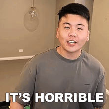 a man in a gray shirt is standing in front of a sign that says `` it 's horrible '' .