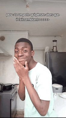 a young man covering his mouth with his hands in front of a blender and a stove