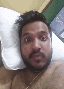 a man with a beard is laying on a bed with a white pillow and a sign that says oprah in the background