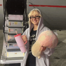 a woman holding a pink cup and a stuffed animal stands in front of a staircase that says exit