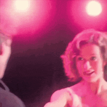 a woman in a pink dress is dancing on a stage in front of a pink light .