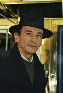 a man wearing a hat and a black coat looks at the camera