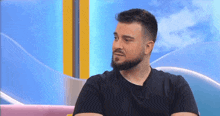 a man with a beard is sitting on a pink couch and talking on a television show .