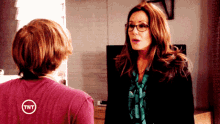 a woman with glasses and a tnt logo on her shirt talks to a boy