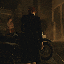 a woman in a black dress stands in front of a motorcycle with a license plate that reads hk