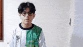a young boy wearing glasses and a white and green nike shirt is standing in front of a white wall .