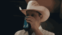a man in a cowboy hat drinking from a blue can