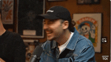 a man wearing a hat and a denim jacket is sitting in front of a microphone .