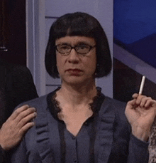 a woman wearing glasses and a blue sweater is smoking a cigarette