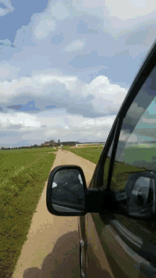 a car is driving down a dirt road with a reflection in the rear view mirror