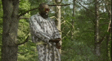 a man with a beard and sunglasses stands in the woods