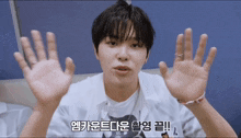 a young man holds up his hands in front of a blue wall with korean writing on the bottom