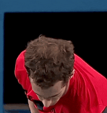 a man in a red shirt is standing in front of a black screen .