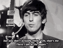 a man in a suit and tie is talking in front of a guitar and says " but you don 't actually think "