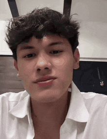a young man wearing a white shirt is looking at the camera .