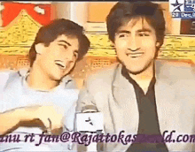 two young men are sitting next to each other on a couch and laughing .