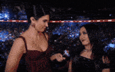 two women standing in front of a crowd with a microphone that says wwe on it