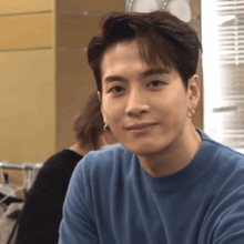 a young man wearing a blue shirt and earrings looks at the camera