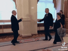 a man in a suit shakes hands with another man and woman