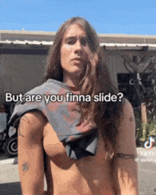 a shirtless man with long hair is standing in front of a building and asking if he is finna slide .