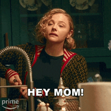 a woman is standing in front of a kitchen sink and says " hey mom "