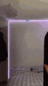 a person is standing next to a bed in a bedroom with a chandelier hanging from the ceiling .