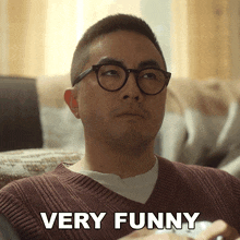 a man with glasses is sitting on a couch with the words very funny below him