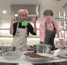 two people in aprons are standing in a kitchen with plates and pots .