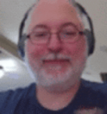 a man with a beard and glasses is wearing headphones and a blue shirt .
