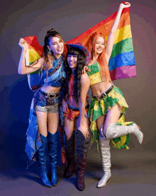three women are posing for a picture while holding up a rainbow flag